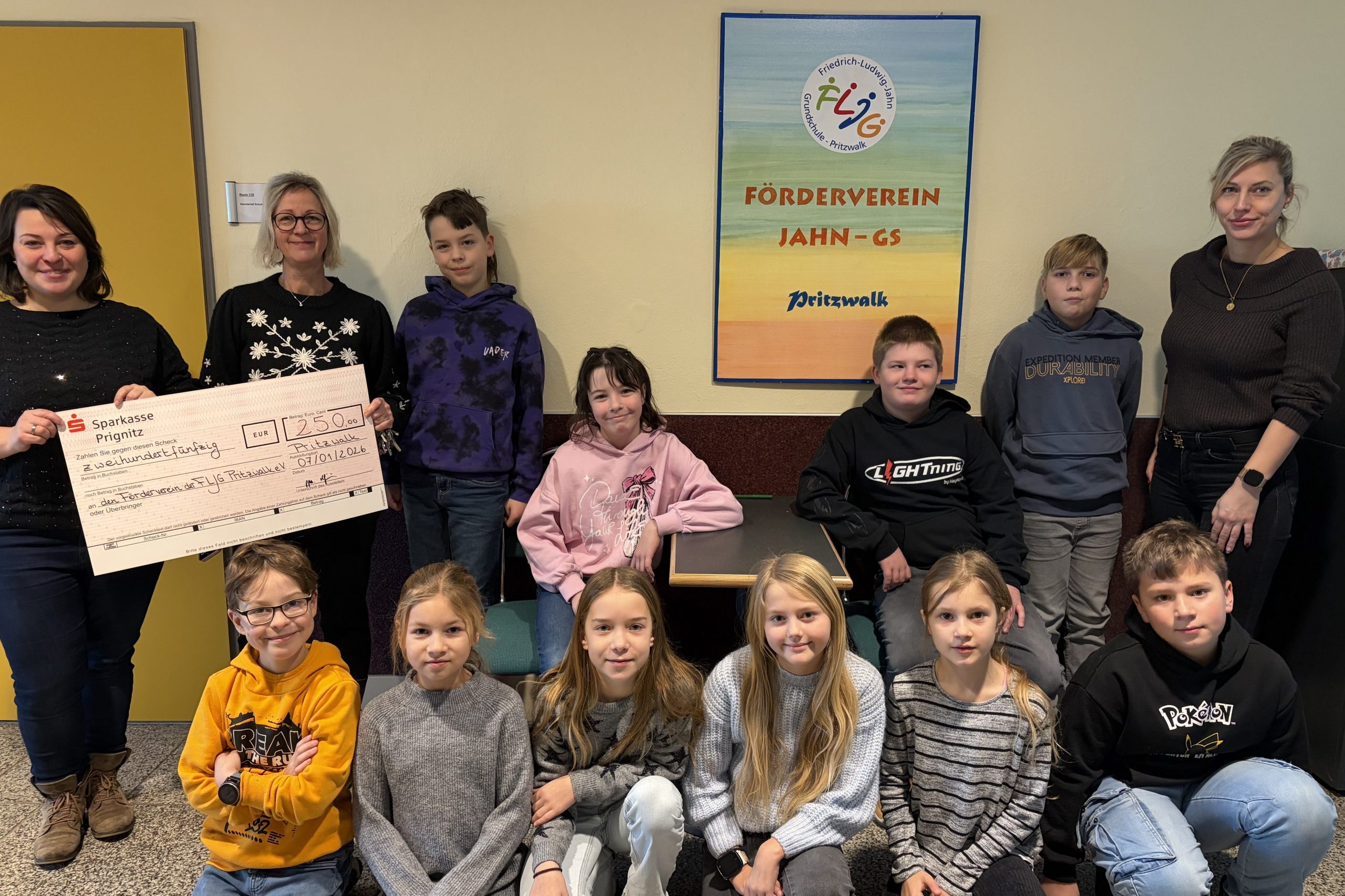 Zwei Vertreterinnen der Stadtwerke Pritzwalk halten den Spendencheck in den Händen. Neben ihnen zeigen sich Schülerinnen, Schüler und eine Lehrerin der FLJ-Grundschule erfreut.